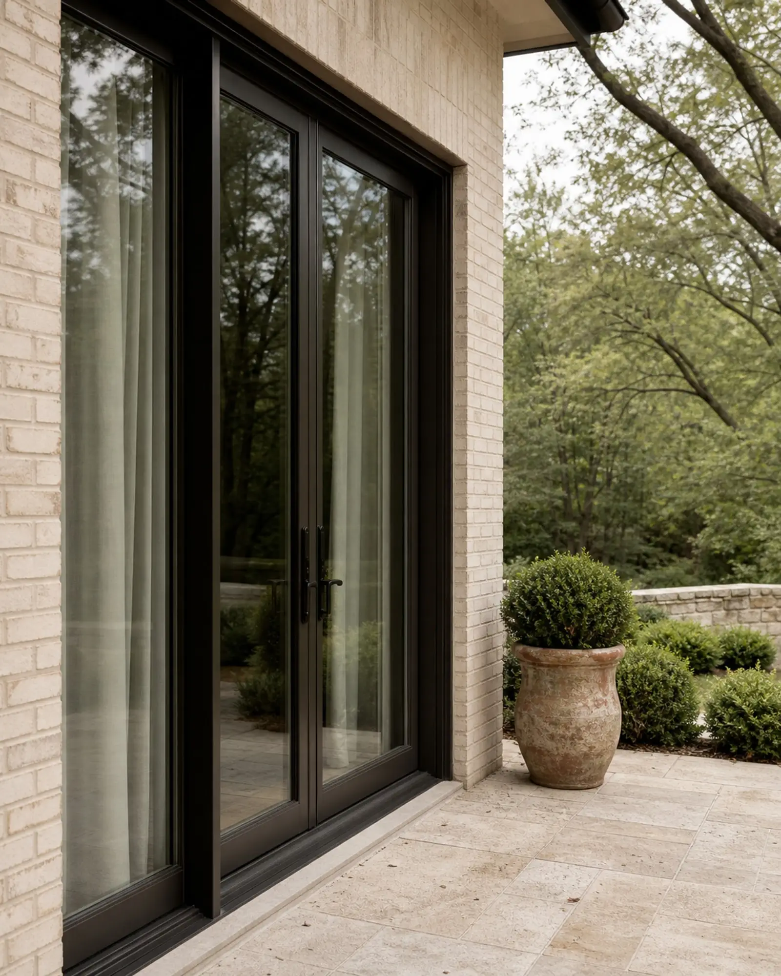 Bronze-black glazed patio doors opening to a limestone terrace and shaded garden — representative concept image