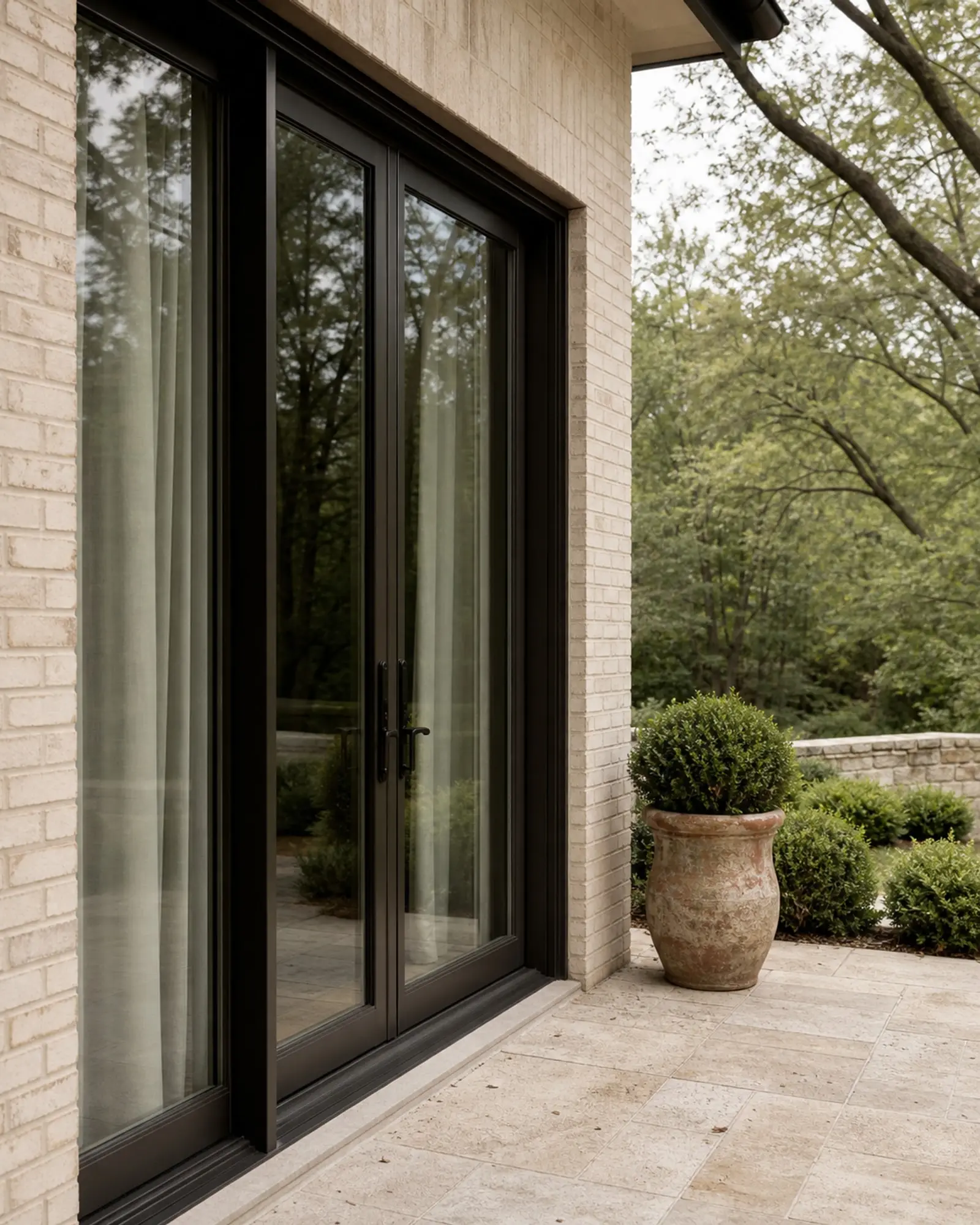 Bronze-black glazed patio doors opening to a limestone terrace and shaded garden (concept image)