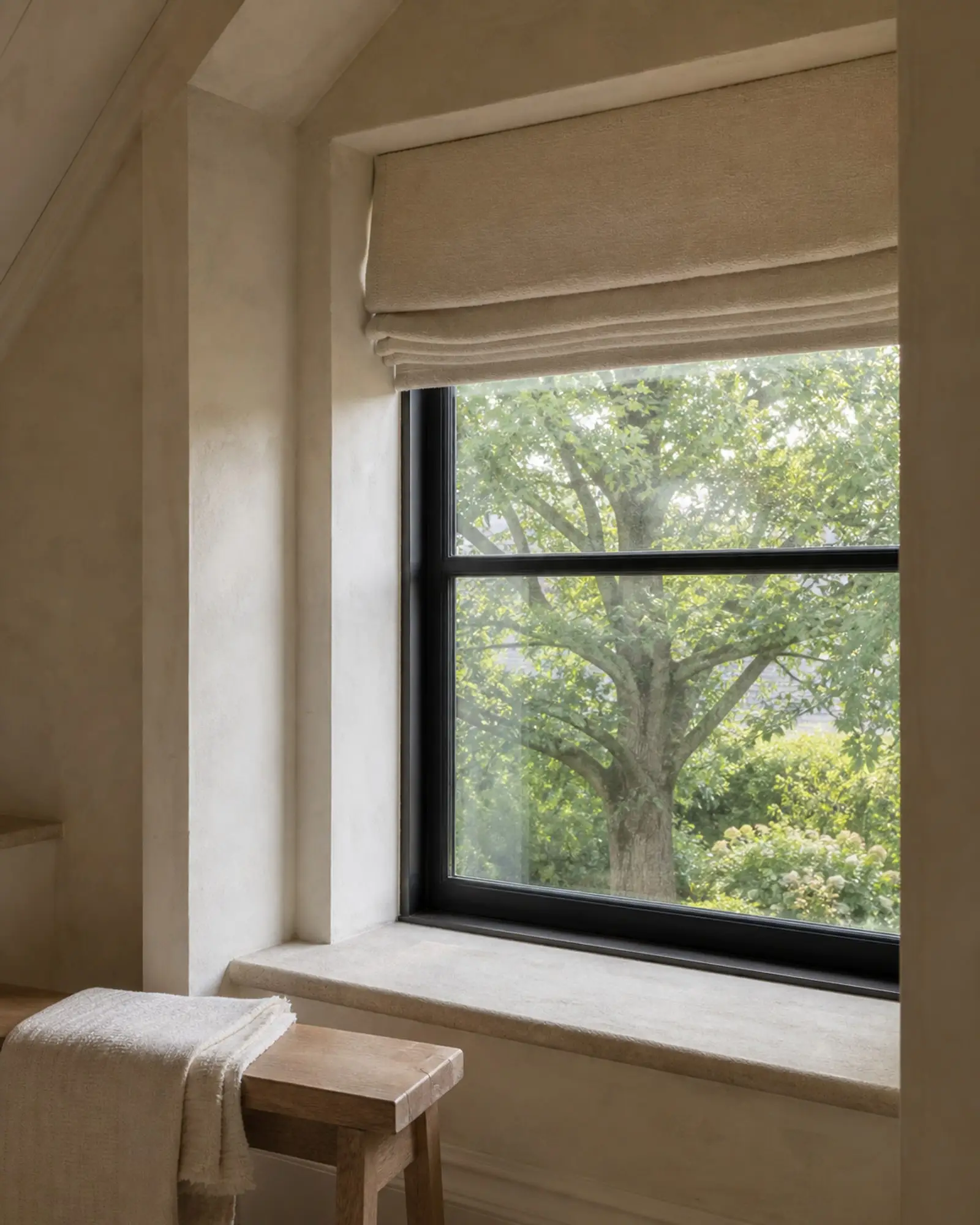 Deep plaster window alcove with a black frame, limestone sill, and mature oak view — representative concept image